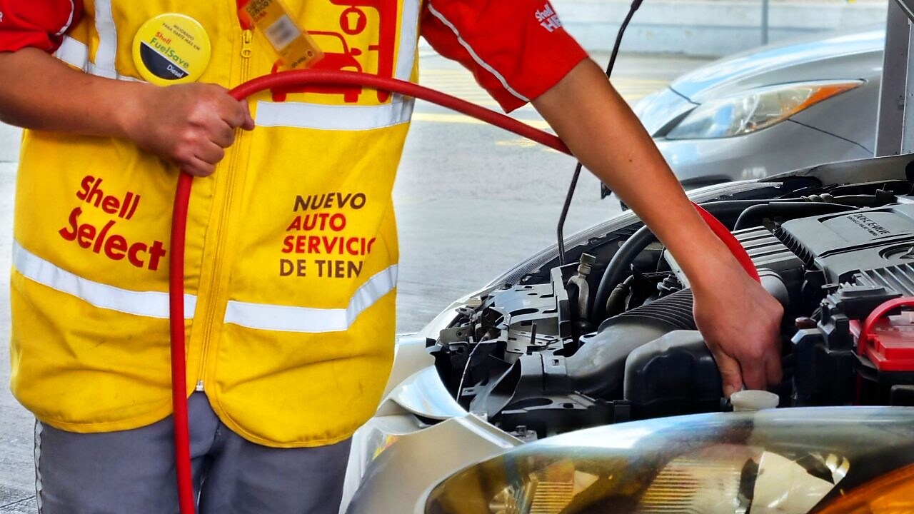 Empleado de la estación Shell, en uniforme amarillo, hace mantenimiento en el automóvil