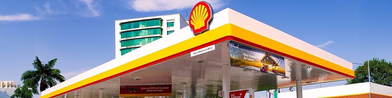 Hombre blanco com su coche Ferrari rojo en una estación de servicio de Shell