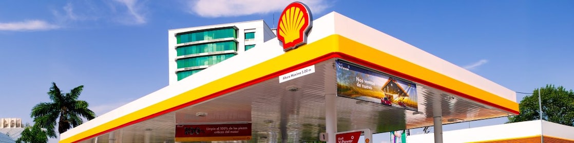 Hombre blanco com su coche Ferrari rojo en una estación de servicio de Shell