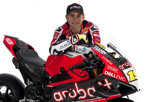 Alvaro Bautista, hombre blanco con ojos azules, en su uniforme de Ducati, veste una gorra y posa con su moto