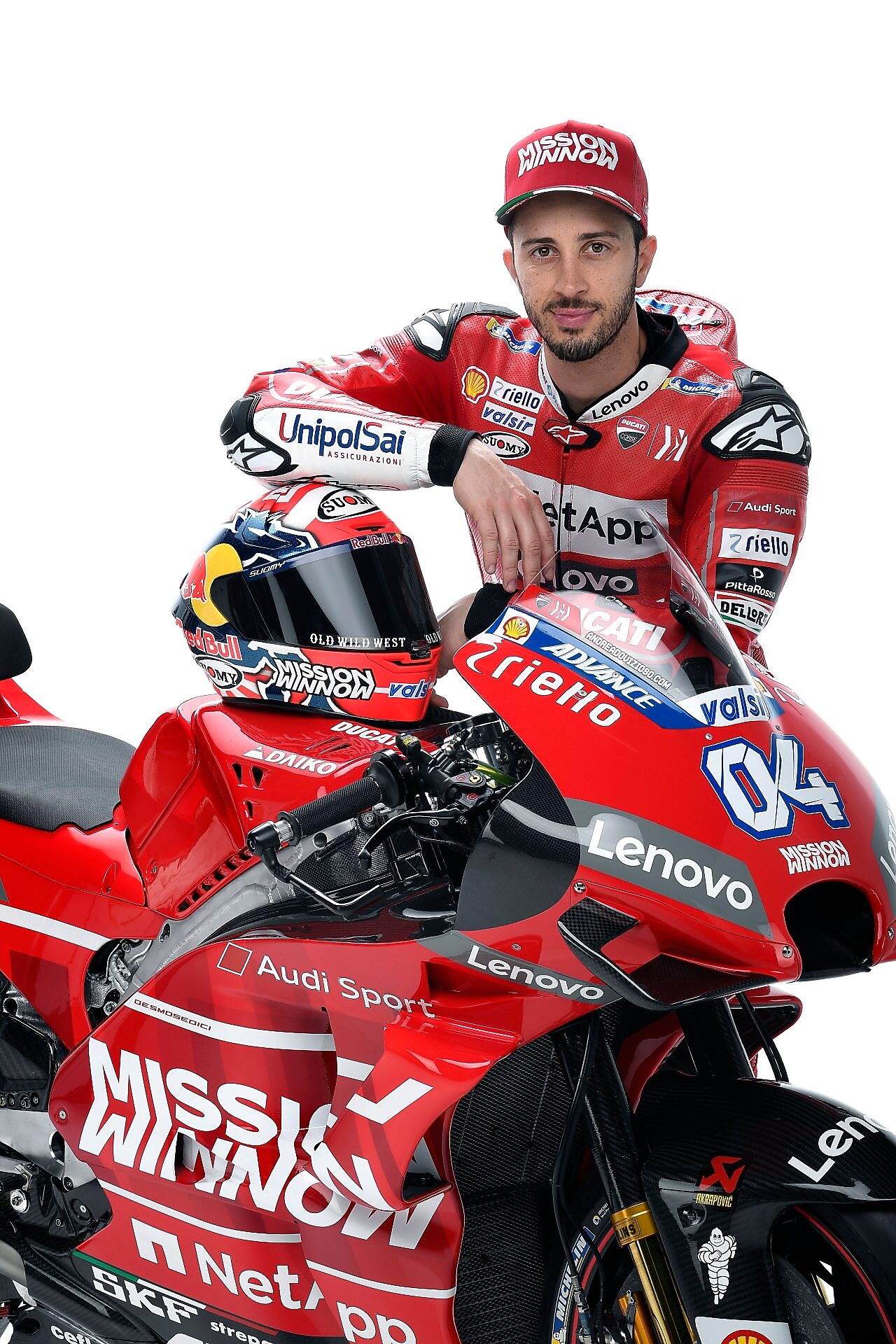 Andrea Dovizioso, hombre blanco con barba negra, en su uniforme de equipo Ducati, veste una gorra y posa con su moto