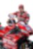Andrea Dovizioso, hombre blanco con barba negra, en su uniforme de equipo Ducati, veste una gorra y posa con su moto