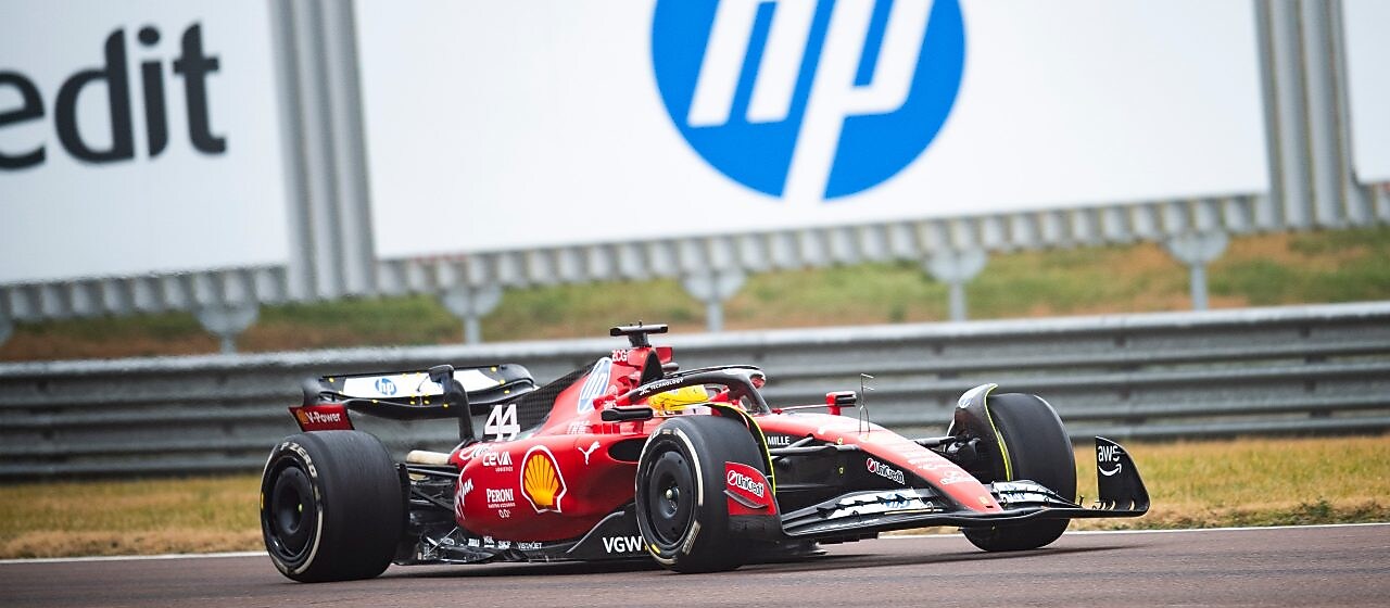 Coche de Ferrari en una carretera, con edificios y montaña al fondo