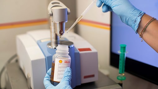 Una mano con guante de laboratorio trabaja en una botella escrita “Shell Helix”