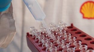 Mano con guante de laboratorio trabajando en viales con líquido transparente